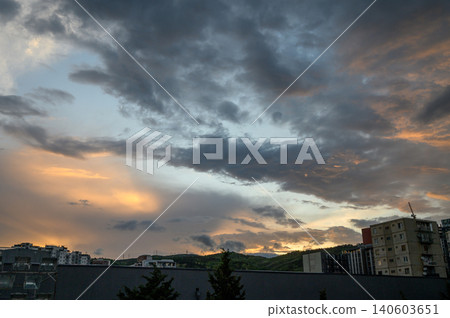 Urban landscape with dramatic cloudy sky at sunset building silhouettes and hilly terrain on horizon Urban landscape with dramatic cloudy sky at sunset building silhouettes and hilly terrain on horizon 140603651