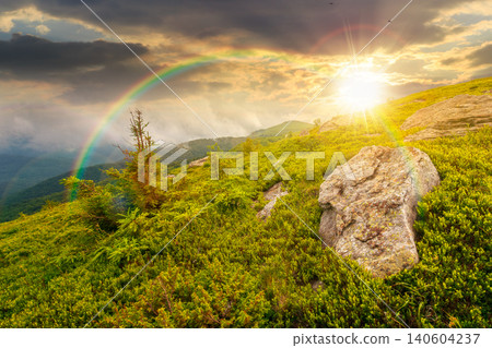sunset over green landscape of mountain in summer. view of rock among grass on the hillside. travel background under a cloudy sky. mountain scenery with rolling hills. weather with rainbow sunset over green landscape of mountain in summer. view of rock among grass on the hillside. travel background under a cloudy sky. mountain scenery with rolling hills. weather with rainbow 140604237