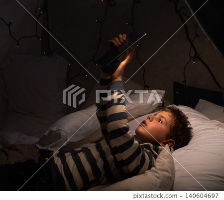 Child, tablet and watch in tent at night for movies, film or cartoon on holiday or vacation in dark room. Boy or kid by fairy lights, pillows and relax at home on digital technology or reading ebook Child, tablet and watch in tent at night for movies, film or cartoon on holiday or vacation in dark room. Boy or kid by fairy lights, pillows and relax at home on digital technology or reading ebook 140604697