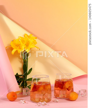 Modern still life with lily flowers and cocktail or tea with apricot, peach and ice cubes on a sunny background,summer party concept, minimalist abstract background for alcoholic beverage presentation Modern still life with lily flowers and cocktail or tea with apricot, peach and ice cubes on a sunny background,summer party concept, minimalist abstract background for alcoholic beverage presentation 140605475