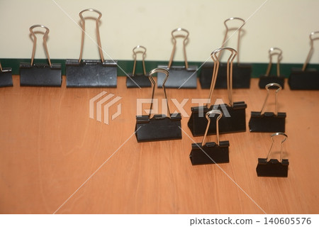 Assorted black metal binder clips arranged on a wooden desk surface Assorted black metal binder clips arranged on a wooden desk surface 140605576
