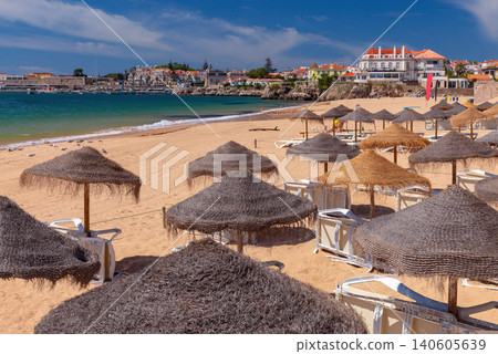 Sandy beach with traditional straw umbrellas and waterfront buildings in Cascais on the Atlantic coast of Portugal. Sandy beach with traditional straw umbrellas and waterfront buildings in Cascais on the Atlantic coast of Portugal. 140605639