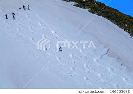 Spring backcountry skiing: Skiers carve tracks on snow-covered slopes under a blue sky. 140605688