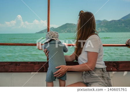 Young mother supporting child standing on boat bench looking at lake landscape travel horizontal photo 140605761