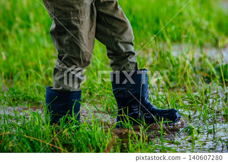 Boy in rubber boots walking on wet grass after the rain Boy in rubber boots walking on wet grass after the rain 140607280