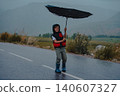 Boy standing on the road trying to hold an umbrella in rainy windy weather 140607327