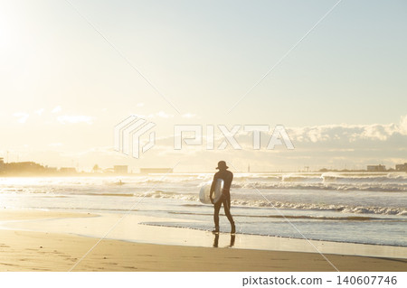 湘南久沼海灘:沐浴在晨光中的衝浪者們沿著海灘漫步。 湘南久沼海灘:沐浴在晨光中的衝浪者們沿著海灘漫步。 140607746