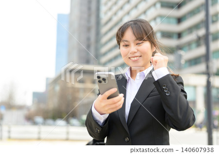 A Japanese woman in her 20s working in an office happily looking at her smartphone. A Japanese woman in her 20s working in an office happily looking at her smartphone. 140607938