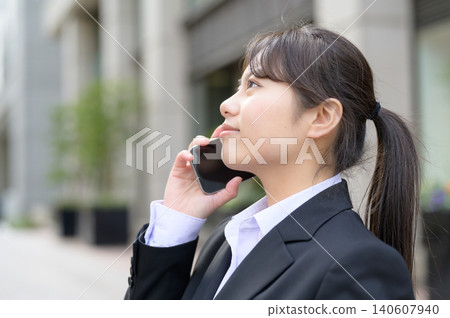 Japanese female office worker in her 20s making a phone call on her smartphone. Japanese female office worker in her 20s making a phone call on her smartphone. 140607940