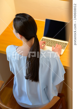 A woman's back as she operates a laptop computer. 140608012