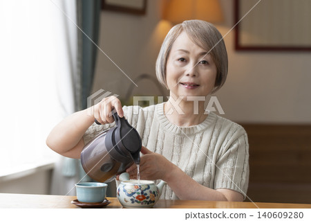 Senior woman pouring tea in the dining room Senior woman pouring tea in the dining room 140609280