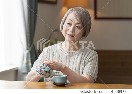 Senior woman pouring tea in the dining room Senior woman pouring tea in the dining room 140609283