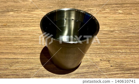 A metal glass of water placed on a wood-grain table. A metal glass of water placed on a wood-grain table. 140610741