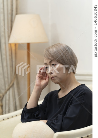 一位老婦人坐在客廳沙發上,雙手抱頭,似乎身體不適。 一位老婦人坐在客廳沙發上,雙手抱頭,似乎身體不適。 140610845
