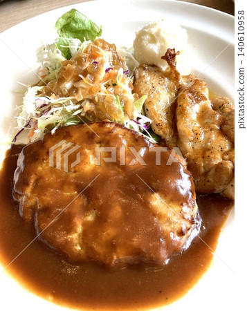 A luxurious plate featuring hamburger steak with demi-glace sauce and grilled chicken with soy sauce. A luxurious plate featuring hamburger steak with demi-glace sauce and grilled chicken with soy sauce. 140610958