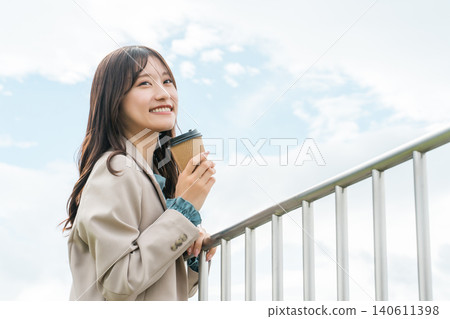 A young Asian woman in a suit drinking coffee on the rooftop to refresh herself A young Asian woman in a suit drinking coffee on the rooftop to refresh herself 140611398