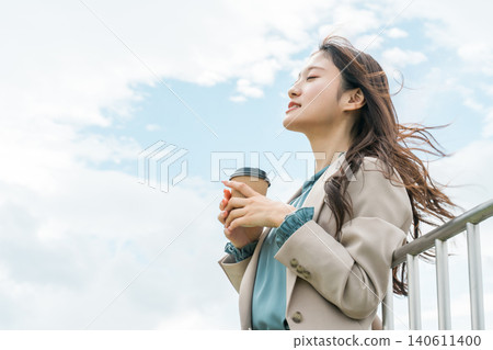 A young Asian woman in a suit drinking coffee on the rooftop to refresh herself 140611400
