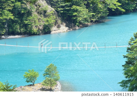 People crossing the dream suspension bridge over the sparkling blue lake of Sumatakyo Gorge. People crossing the dream suspension bridge over the sparkling blue lake of Sumatakyo Gorge. 140611915
