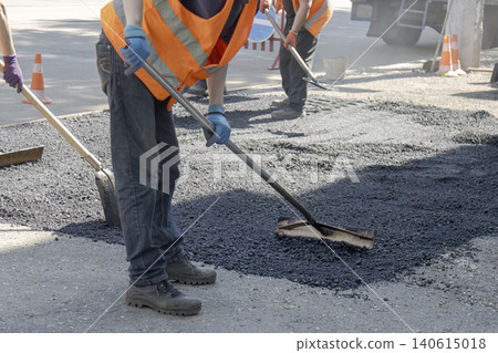 Road construction workers in safety vests spreading and leveling fresh asphalt on a city street Road construction workers in safety vests spreading and leveling fresh asphalt on a city street 140615018