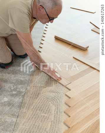 Carpenter installing herringbone wooden parquet planks during flooring work in apartment renovation Carpenter installing herringbone wooden parquet planks during flooring work in apartment renovation 140617263