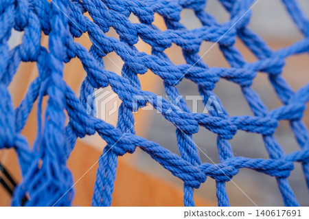 Close-up of a tightly woven blue rope net with thick braided cords and knotted junctions Close-up of a tightly woven blue rope net with thick braided cords and knotted junctions 140617691
