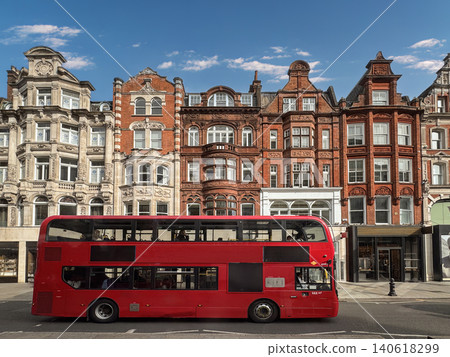 Red Double Decker Bus on London Street With Historic Brick Architecture and Blue Sky 140618299