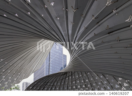 a stylized architectural feature located outside The Ring Shopping Center in Chongqing, China. Overlapping metal panels form a dramatic, twisting vortex structure. The custom-cut triangular venting 140619207