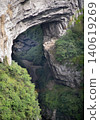 Nestled deep within a colossal limestone gorge of the Wulong Karst in Chongqing, China, the ancient Tianfu Official Post Station rests peacefully beneath the towering span of the magnificent Tianlong 140619269