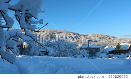 A picturesque winter landscape in a rural or suburban area on a bright, sunny day. The area around the houses is filled with trees and bushes, which appear completely white due 140620013
