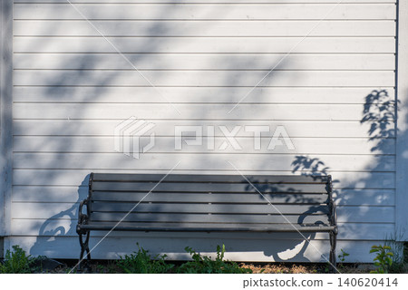 black metal garden bench against white wooden wall with tree shadows black metal garden bench against white wooden wall with tree shadows 140620414