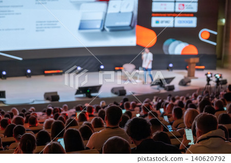 Audience watching speaker on stage at busy tech conference in large auditorium Audience watching speaker on stage at busy tech conference in large auditorium 140620792
