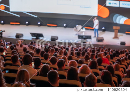 Conference audience listening to presenter on stage during business seminar with large screen and lighting Conference audience listening to presenter on stage during business seminar with large screen and lighting 140620804