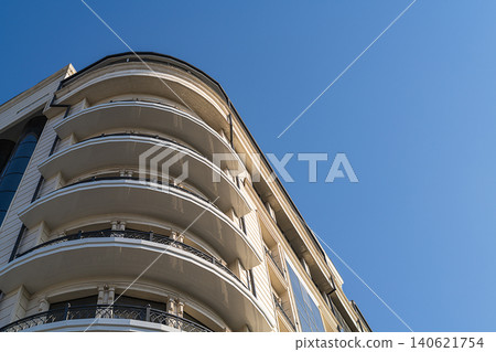 Bottom view of multi-storey building with round corner, panoramic balconies with 270-degree view against background of clear blue sky. Architectural elements in modern urban planning, building Bottom view of multi-storey building with round corner, panoramic balconies with 270-degree view against background of clear blue sky. Architectural elements in modern urban planning, building 140621754