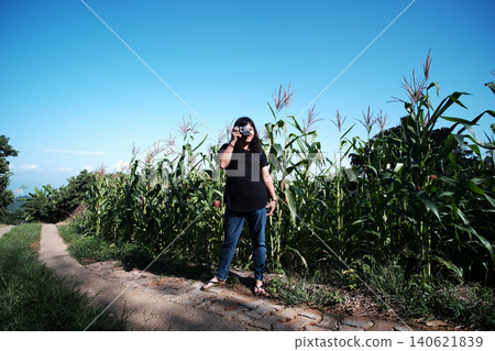 Happy Asian woman taking a photo with analog film camera corn fields with blue sky for travel and journey in Thailand Happy Asian woman taking a photo with analog film camera corn fields with blue sky for travel and journey in Thailand 140621839