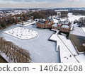 Aerial view of a snow-covered modern horse farm and countryside ranch with a frozen pond, stables, and paddocks near a suburban town in Gelderland, Netherlands. 140622608