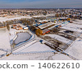 Aerial view of a snow-covered modern horse farm and countryside ranch with a frozen pond, stables, and paddocks near a suburban town in Gelderland, Netherlands. 140622610