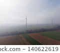 Aerial view of industrial wind turbines standing in misty green and brown agricultural fields under bright morning sun fog in the Dutch countryside, Netherlands. 140622619