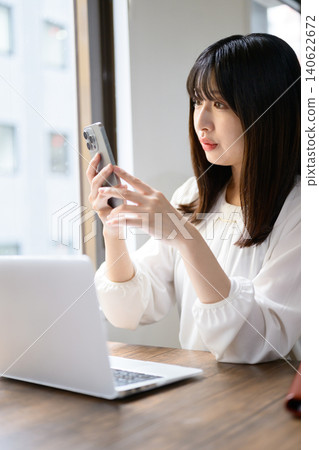 Japanese woman working in the office using a laptop and smartphone. Japanese woman working in the office using a laptop and smartphone. 140622672