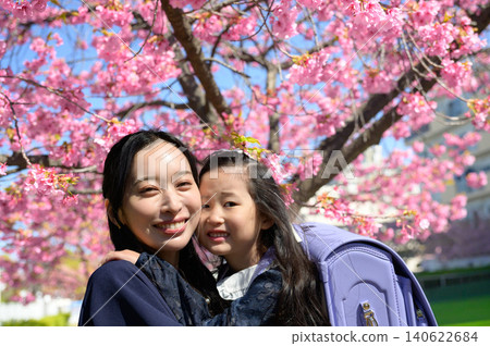 在一棵櫻桃樹下,一位母親擁抱著背著書包的女兒。 在一棵櫻桃樹下,一位母親擁抱著背著書包的女兒。 140622684