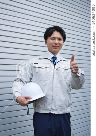 A smiling young man wearing work clothes and holding a helmet. 140624099