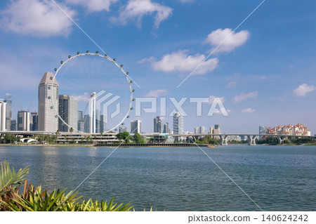 A scenic view of the Singapore skyline featuring the Singapore Flyer Ferris wheel, modern skyscrapers, and waterfront under a bright blue sky. The Marina Reservoir adds to the vibrant urban landscape A scenic view of the Singapore skyline featuring the Singapore Flyer Ferris wheel, modern skyscrapers, and waterfront under a bright blue sky. The Marina Reservoir adds to the vibrant urban landscape 140624242