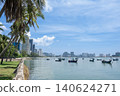 Scenic waterfront view featuring boats on calm water, surrounded by lush palm trees and modern city skyline under a bright blue sky with fluffy clouds 140624271