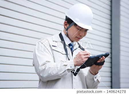 A smiling young man wearing work clothes and a helmet 140624278