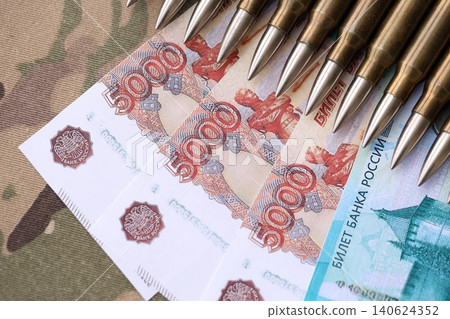 Russian money with bullets on multicam camouflage fabric close up. Concept of russian army funds Russian money with bullets on multicam camouflage fabric close up. Concept of russian army funds 140624352