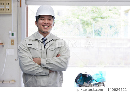 A smiling young man wearing work clothes and a helmet 140624521