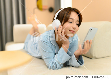 A woman operating a smartphone while relaxing on the sofa A woman operating a smartphone while relaxing on the sofa 140625459