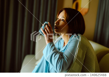 一位女士坐在沙發上用杯子喝水。 140625488