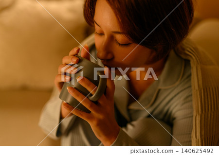 一位女士正在用馬克杯喝熱飲。 140625492