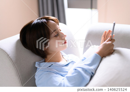 A woman operating a smartphone on the sofa A woman operating a smartphone on the sofa 140625524