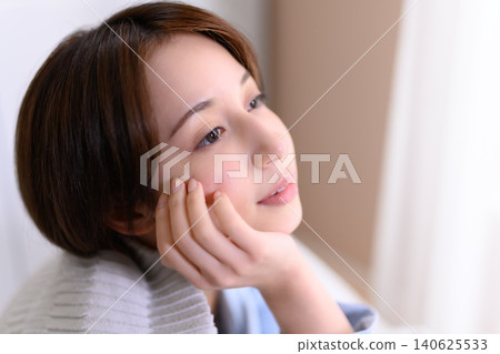 A woman resting her chin on her hand and gazing into the distance. A woman resting her chin on her hand and gazing into the distance. 140625533